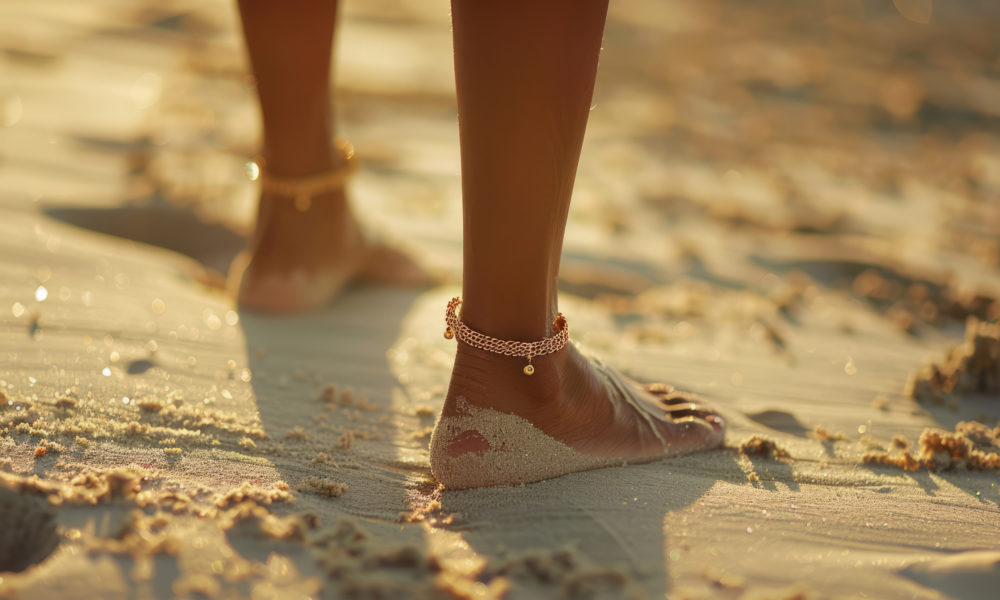 Woman's legs with an metallic golden anklet shimmering in the sunlight on a sandy beach. Generative AI illustration