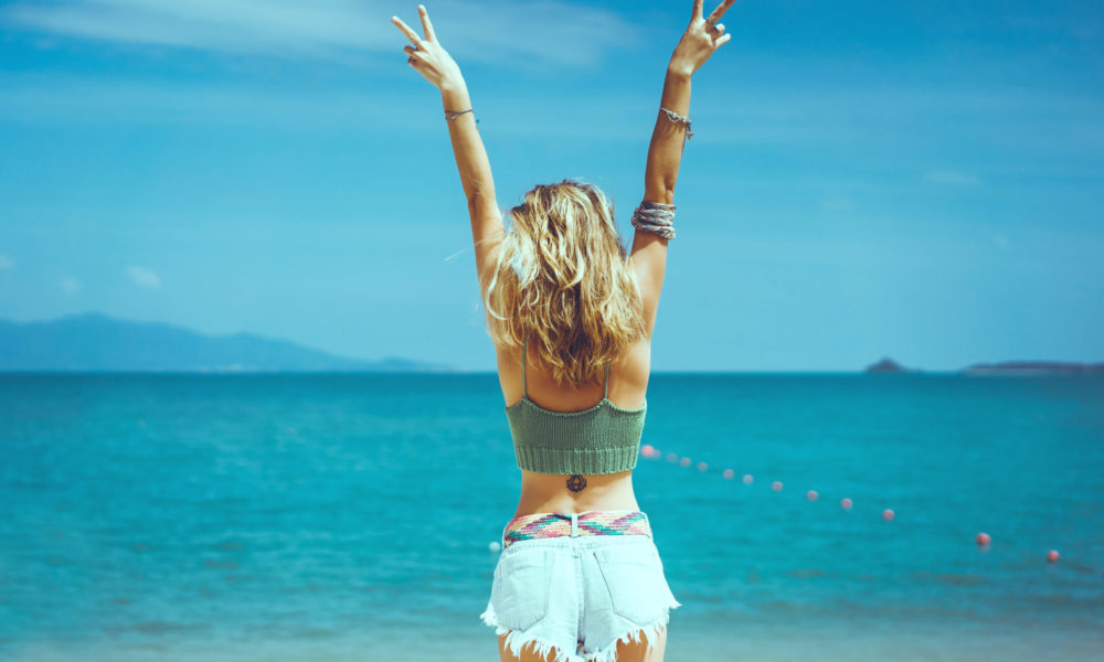 pretty woman posing in the sea, blue sky, hair wild, victory hand up!, outdoor portrait hipster, fashion model, pretty female, denim shorts, hippie, tattoo